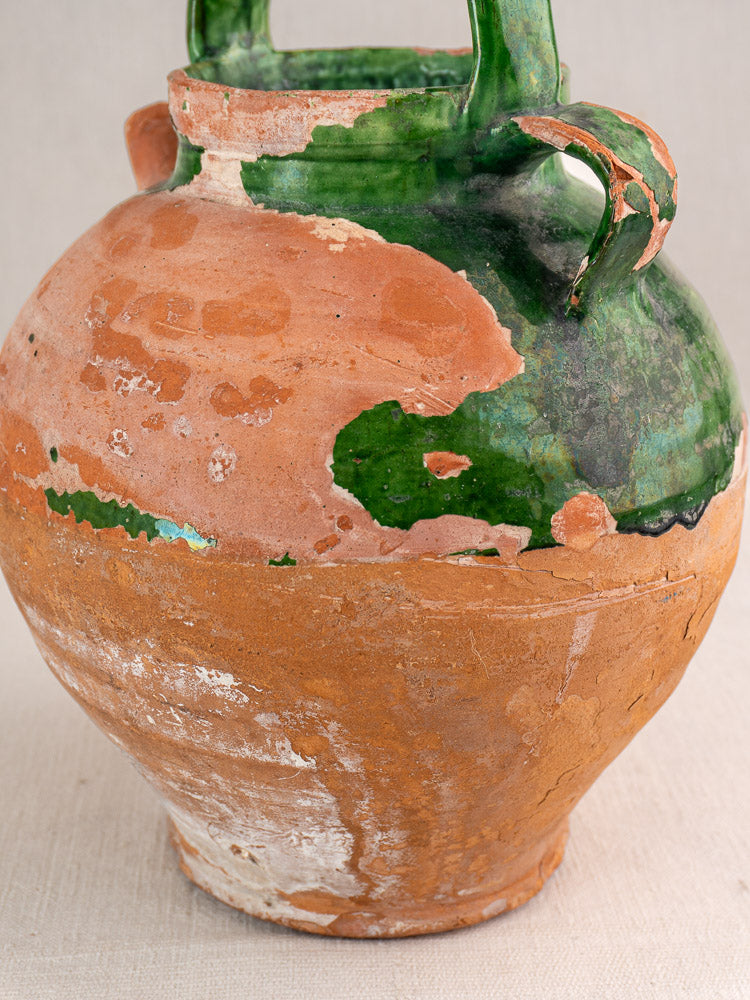 Antique French green glazed earthenware gargoulette with chipped rim and broken handle, clay exposed, on neutral background.