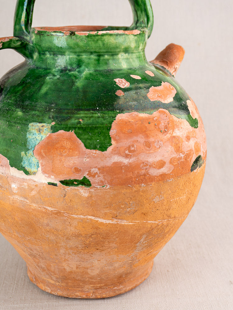Antique French green-glazed earthenware gargoulette with rustic patina, chipped rim, spout, and curved handle.