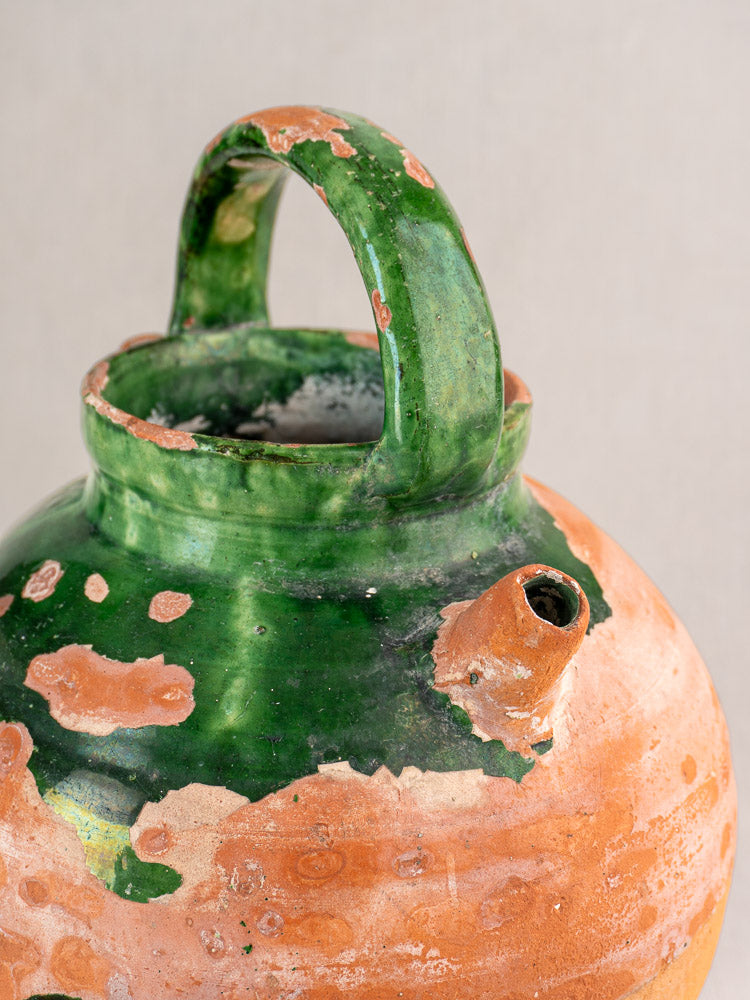 Antique French green glazed earthenware gargoulette with handle, spout, and terracotta chips on neutral background.