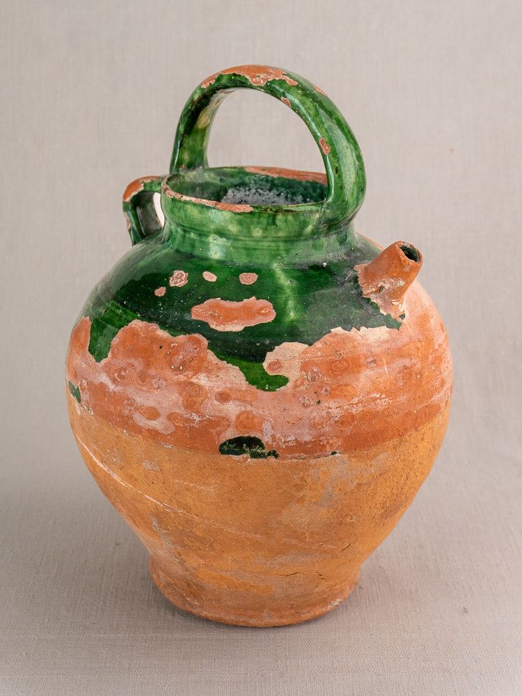 Antique French green-glazed earthenware gargoulette with rounded body, short spout, and arched handle; terracotta base exposed.