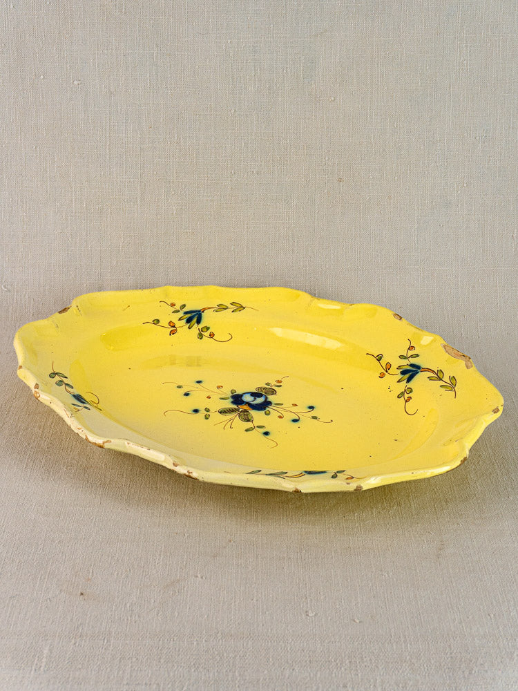 Antique French faience platter, oval yellow earthenware with scalloped edge, blue and green floral motifs, on neutral fabric.