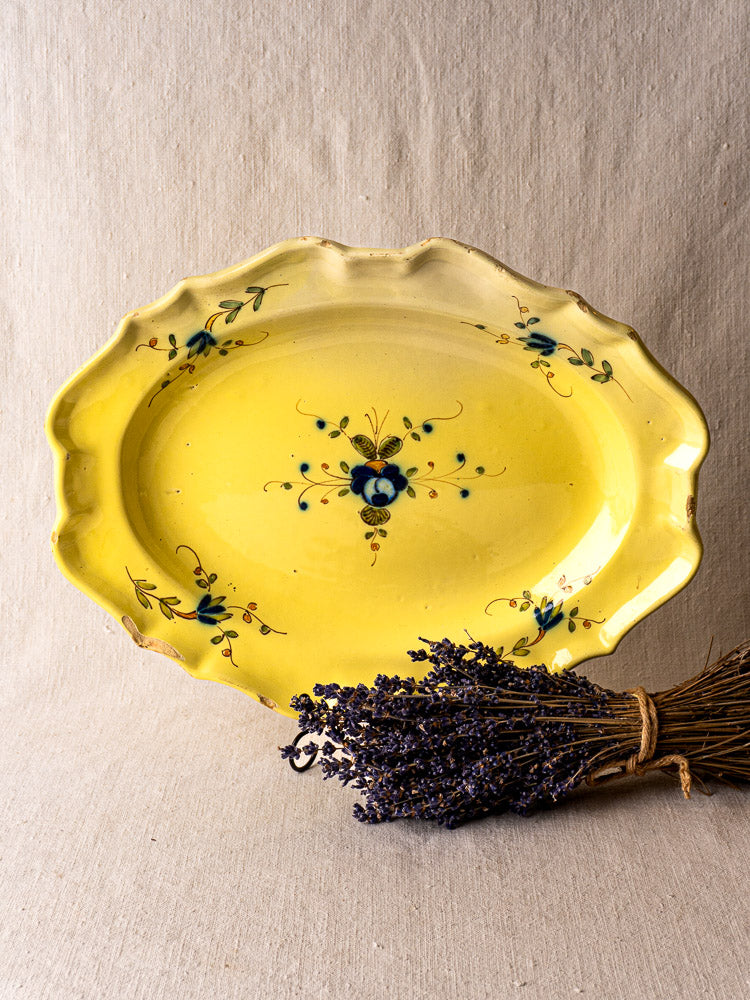 Antique French faience platter with yellow glaze and blue floral motifs, shown on beige fabric with dried lavender.