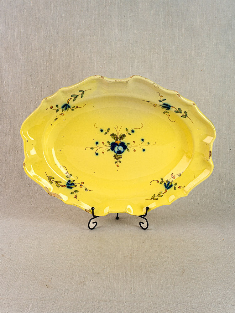 Antique French faience platter with yellow glaze, blue-green floral motif, scalloped edges on black metal stand.