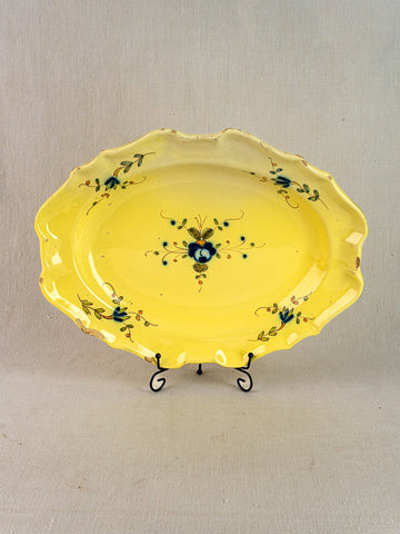 Antique French faience platter with yellow glaze, blue-green floral motif, scalloped edges on black metal stand.