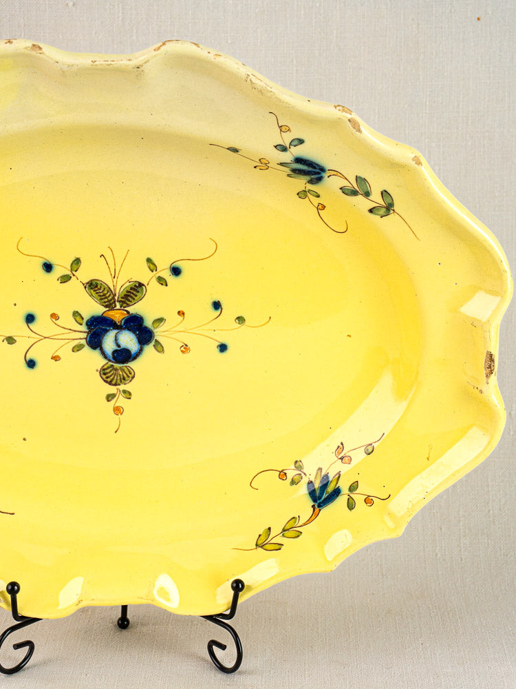 Antique French faience platter with yellow glaze and blue-green floral motifs on a black metal stand.