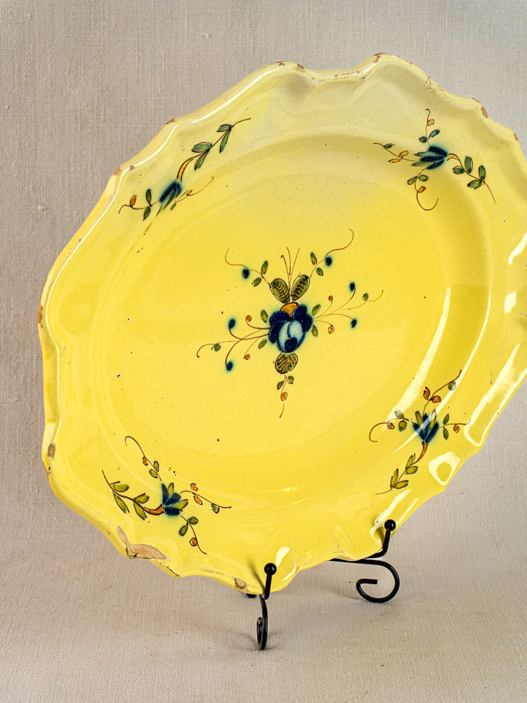 Antique French faience platter with yellow glaze, scalloped edge, blue floral and green leaf motifs on stand.