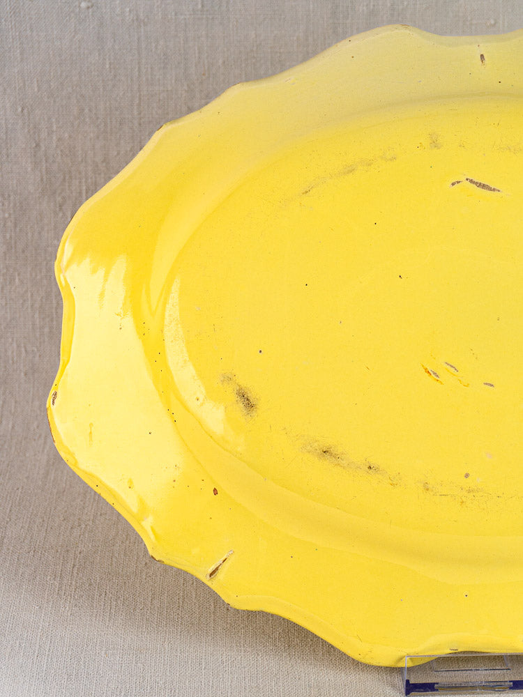 Antique French faience platter, c. 1880–1900, yellow glaze, scalloped edge, light wear; neutral fabric background.