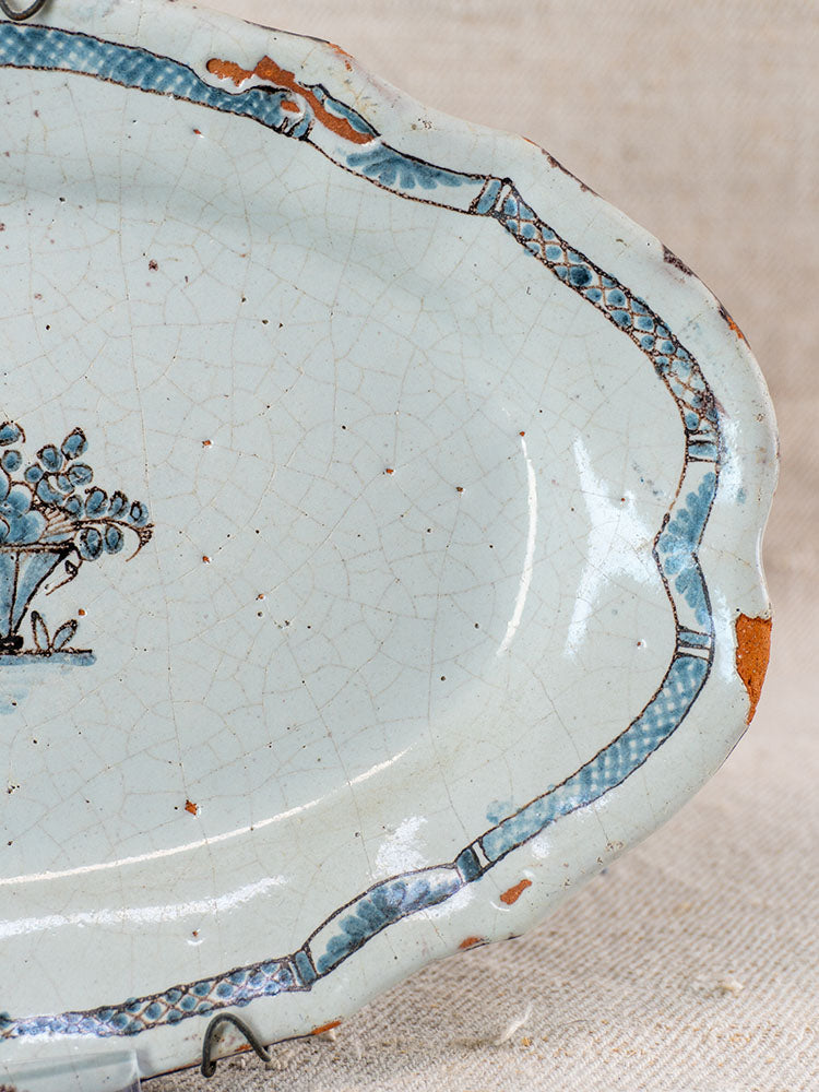 Antique French faience platter with blue border, visible crazing, chips, and simple blue tree motif on textured fabric.