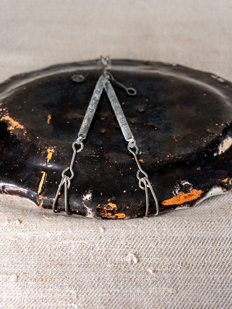Antique French faience Cul Noir platter with metal dividers, dark weathered oval surface, on textured beige fabric.
