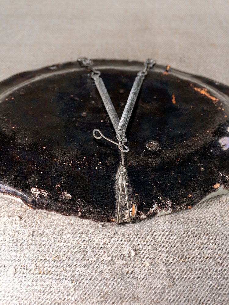 Vintage metal tongs with textured handles on 18th-century French faience platter, displayed on a light textured fabric.