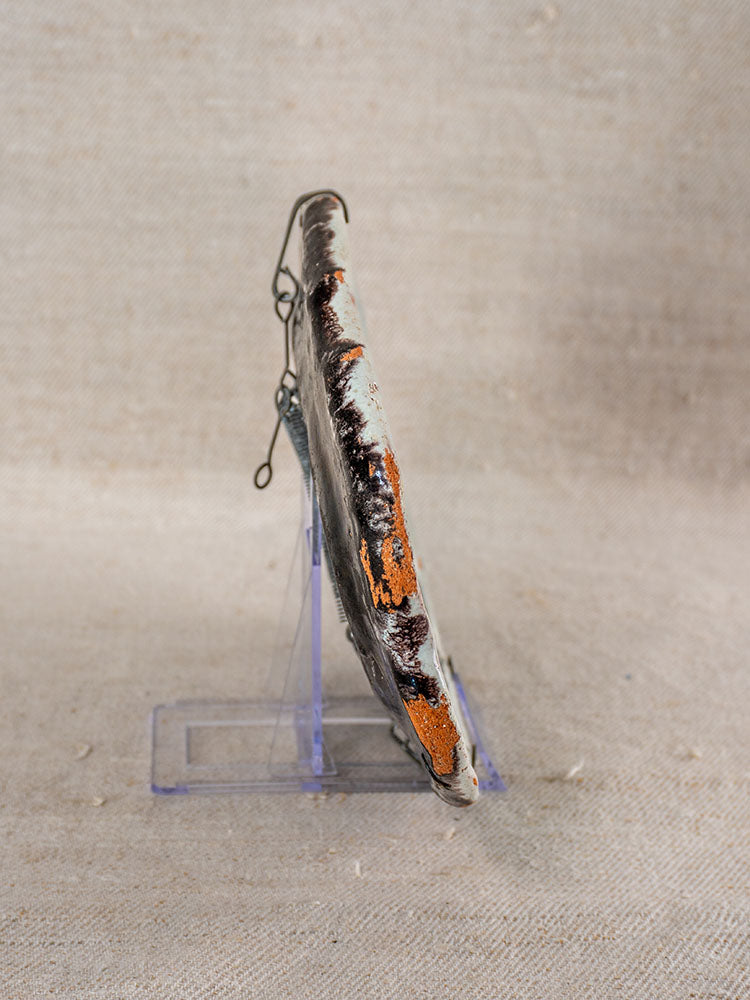 Antique French faience Cul Noir platter, 18th century, rust-orange and white, upright on clear stand, side view.