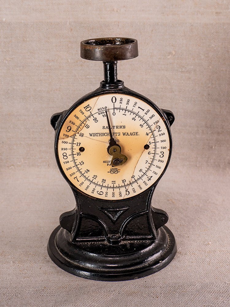 Antique cast iron Salter kitchen scale with ivory dial on neutral fabric background.