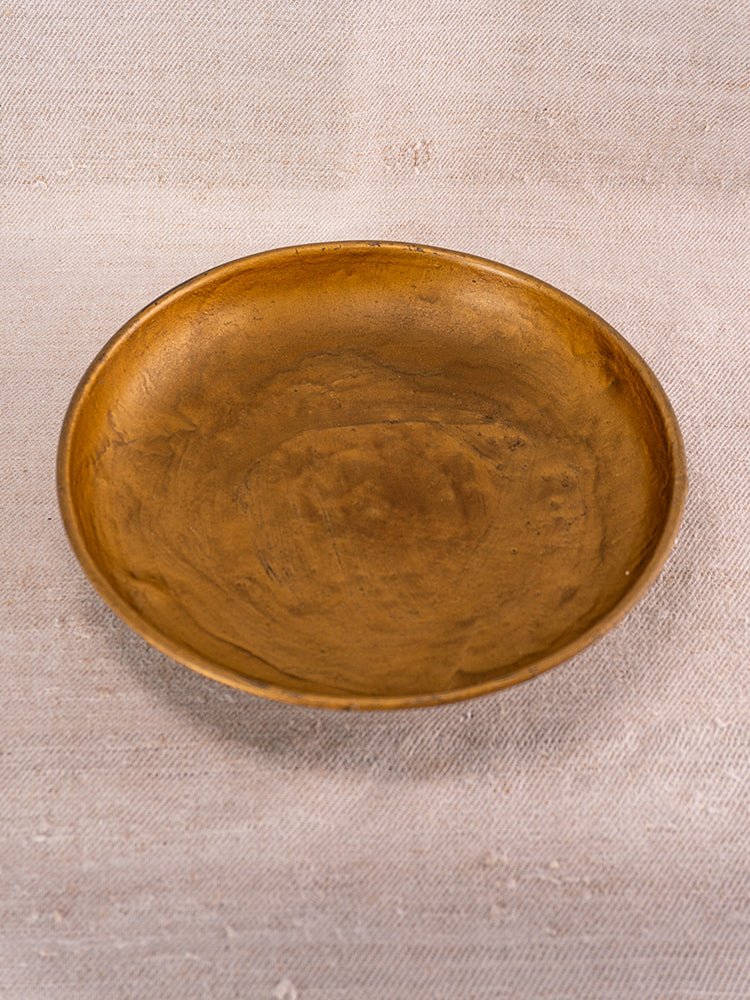 Round shallow brass plate with smooth patina displayed on a textured light fabric backdrop.