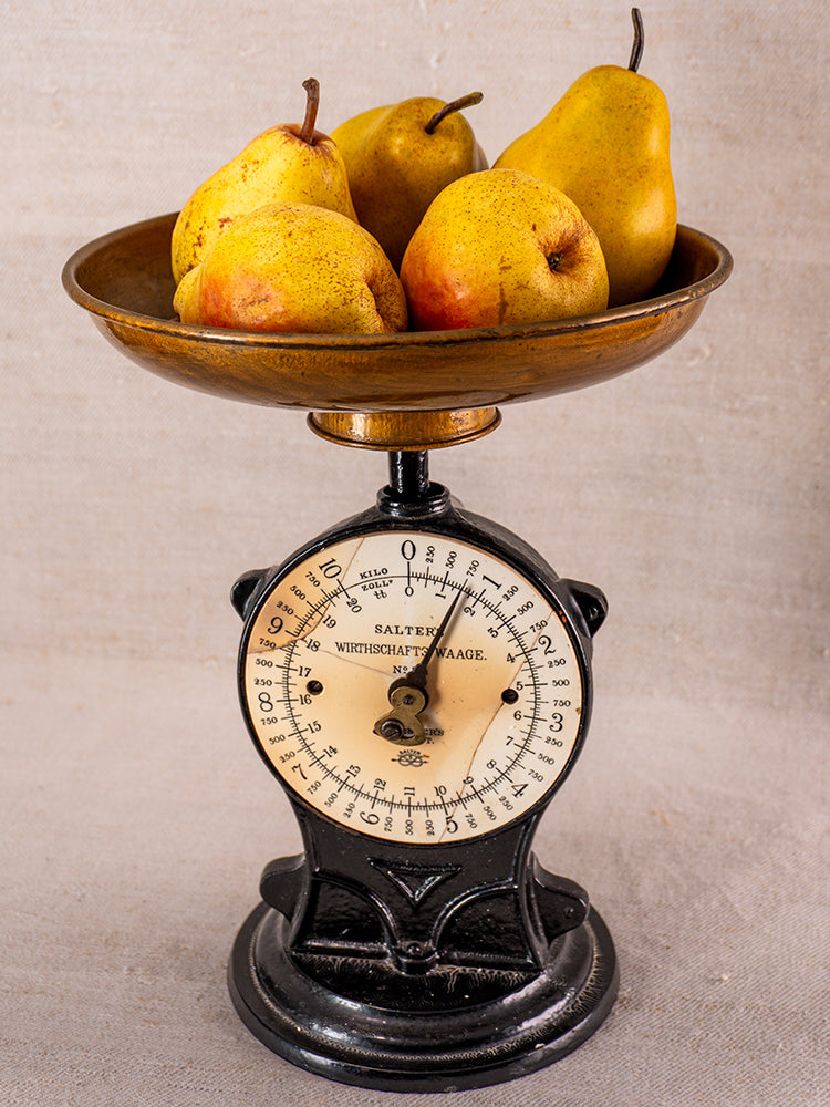 Antique Salter cast iron kitchen scale with black and gold dial, brass pan, on neutral fabric background.
