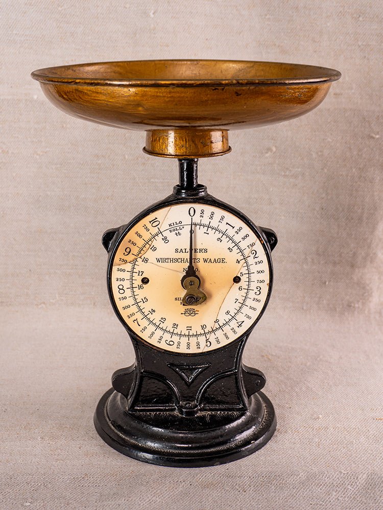 Antique Salter cast iron kitchen scale with black and gold dial, brass pan, on neutral fabric background.