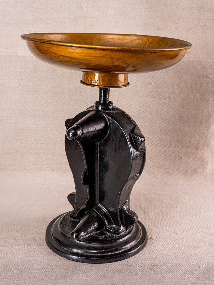 Antique cast iron Salter kitchen scale with round brass pan and ornate black base on neutral fabric.