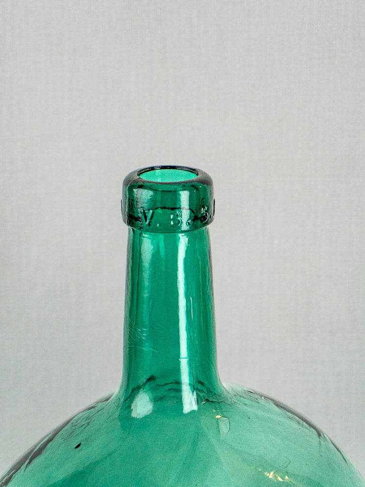 Antique hand-blown Spanish green glass demijohn with raised rim and engraved markings, on gray background.
