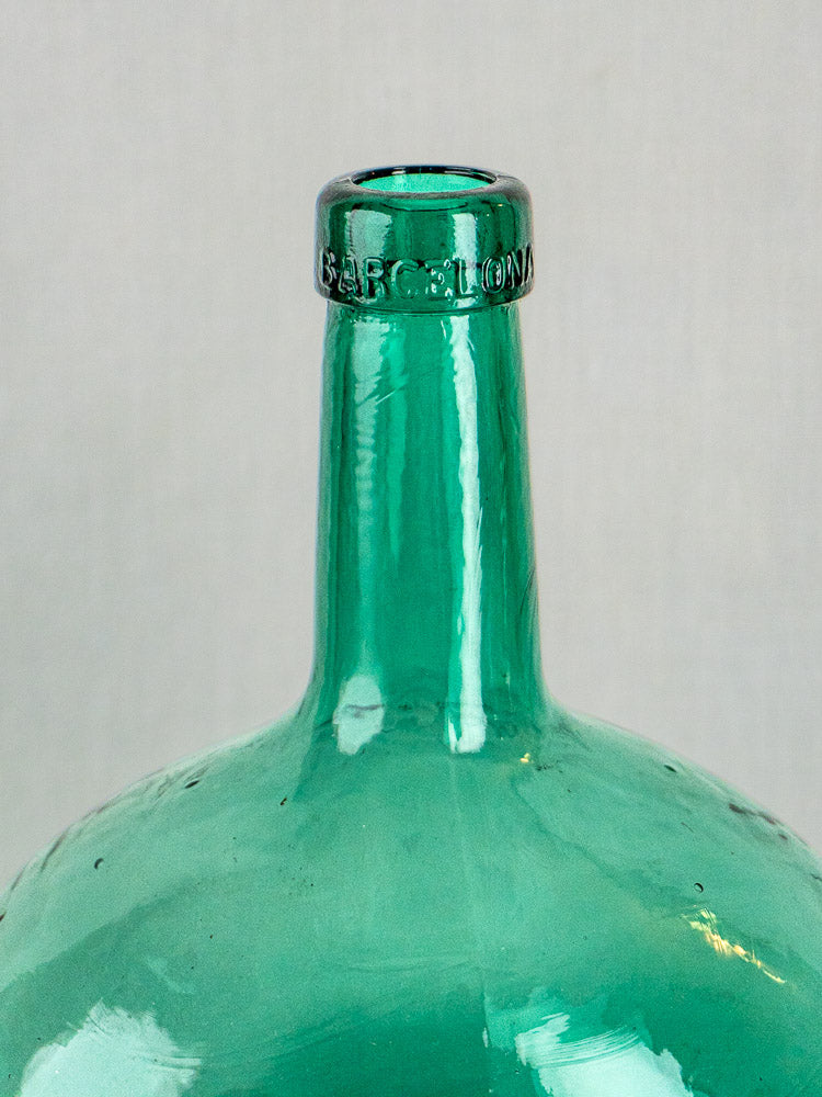 Hand-blown Spanish green glass demijohn with BARCELONA embossed rim, plain light background.