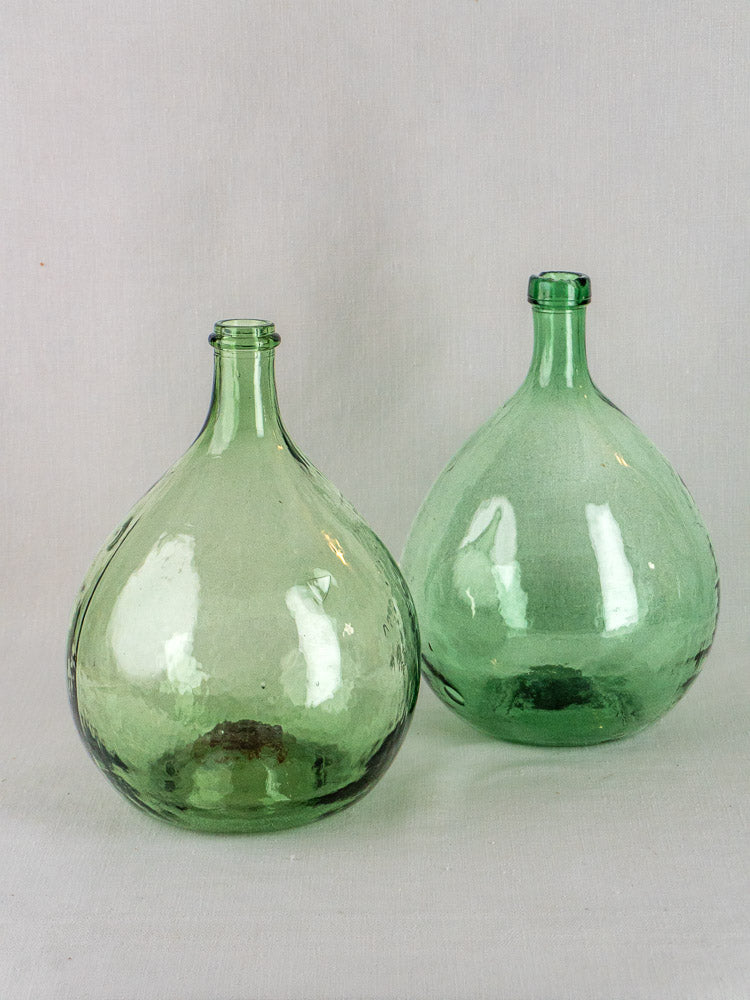 Three large round antique Spanish green glass demijohns displayed side by side on a gray surface.