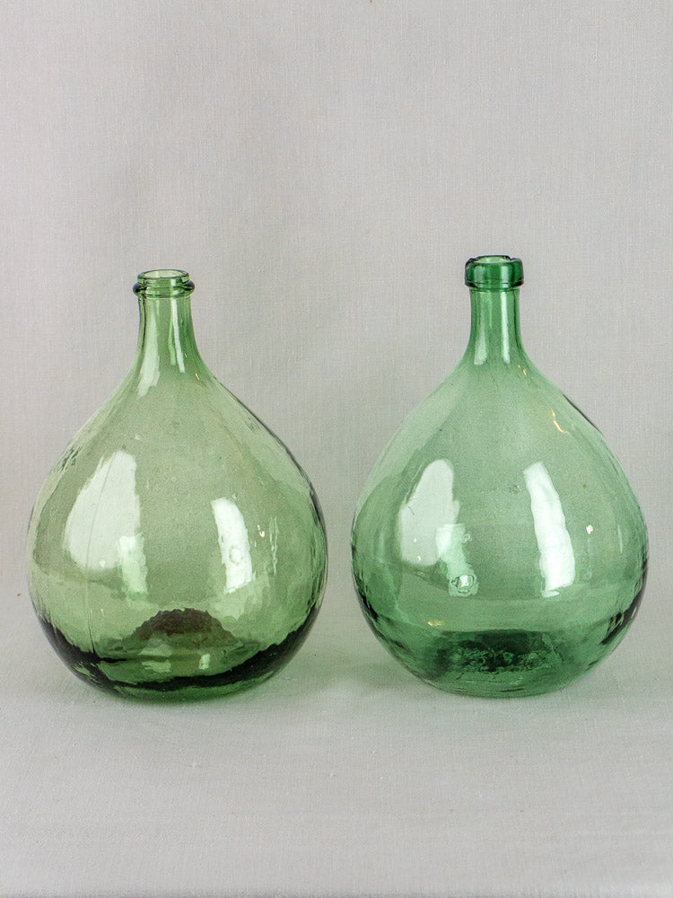 Set of three antique Spanish green glass demijohns displayed on a light gray surface.
