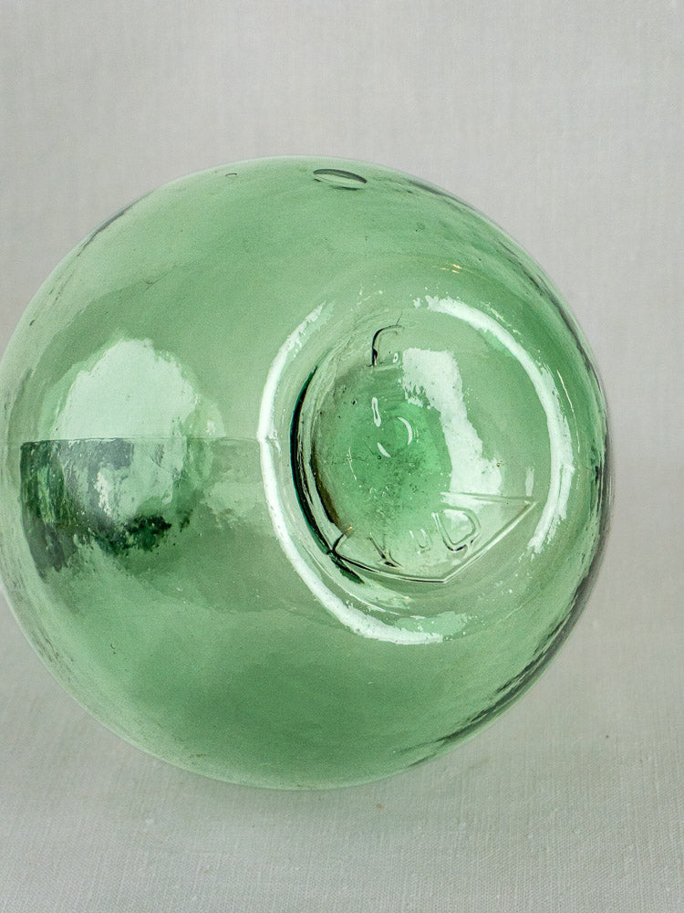 Hand-blown Spanish green glass demijohn with vintage bottle-green hue and circular seal, on light background.
