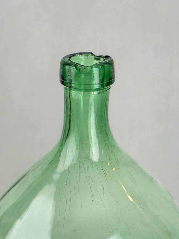 Large Spanish green glass antique demijohn with chipped, uneven rim and faint internal cracks, on light background.