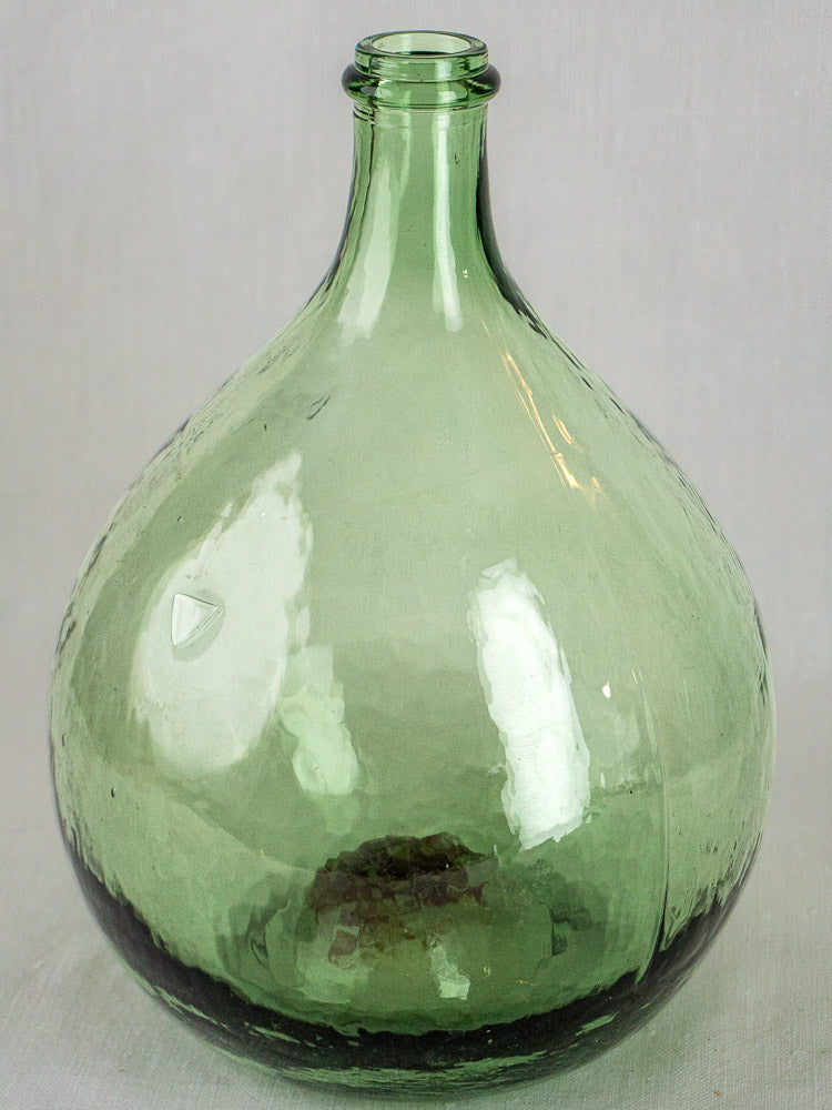 Three large antique hand-blown Spanish green glass demijohns with round bodies and narrow necks on a light background.