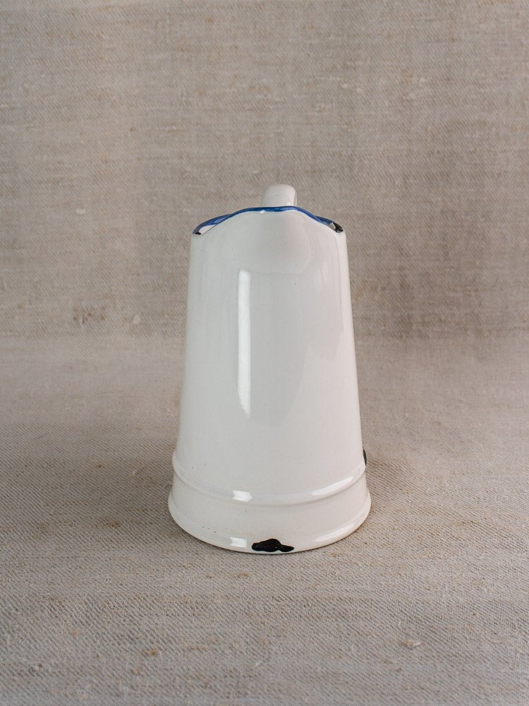 Vintage French faience pitcher with white glaze, blue trim, and minor base chips on beige fabric.