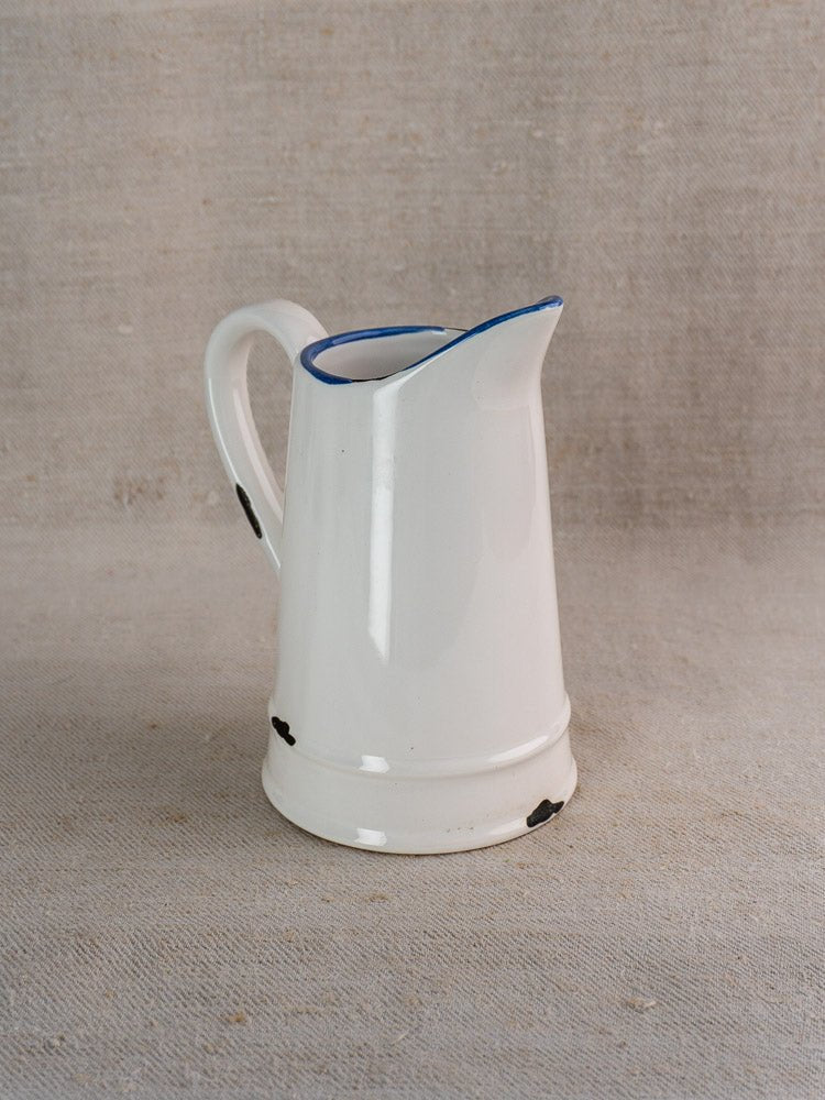 Vintage French faience-style white ceramic pitcher with blue trim, handle, and subtle dark spots near base.