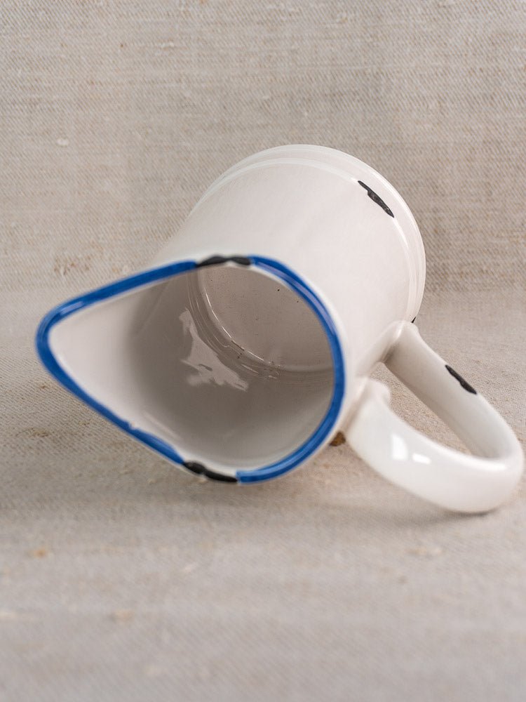 Vintage French faience pitcher with white glaze and blue trim on textured beige surface.
