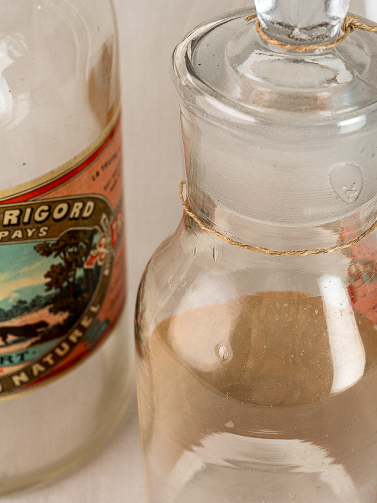 Antique French L. Jaubert truffle jar with vintage label beside a clear glass bottle.