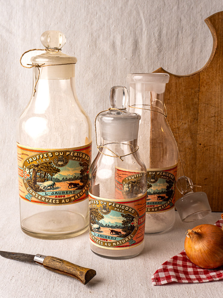 Set of three antique French L. Jaubert truffle jars with corks and Fruits du Perigord labels, arranged by size.