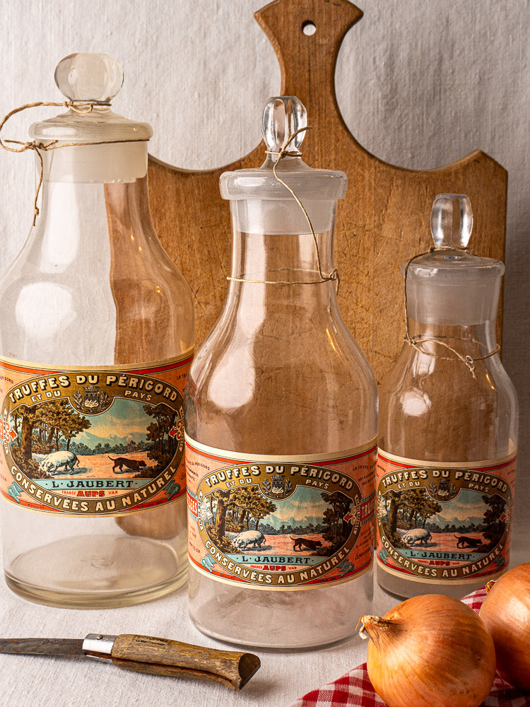 Set of three antique French L. Jaubert truffle jars from Aups, circa 1900, with cutting board, onions, and knife on fabric surface.