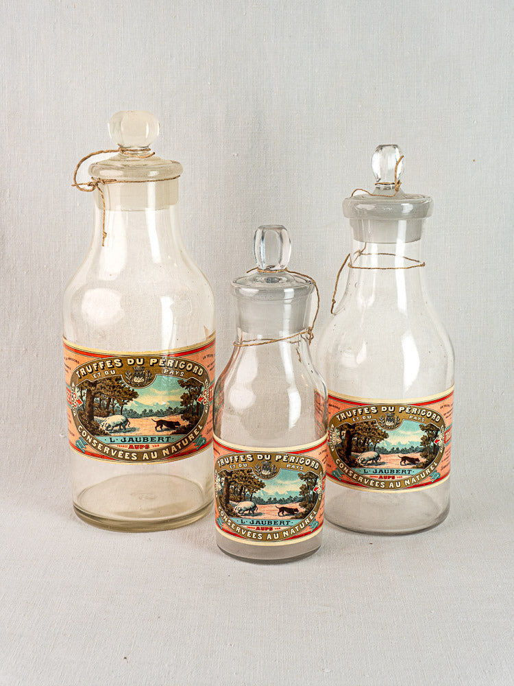 Set of three antique French L. Jaubert truffle jars with corks and Fruits du Perigord labels, arranged by size.