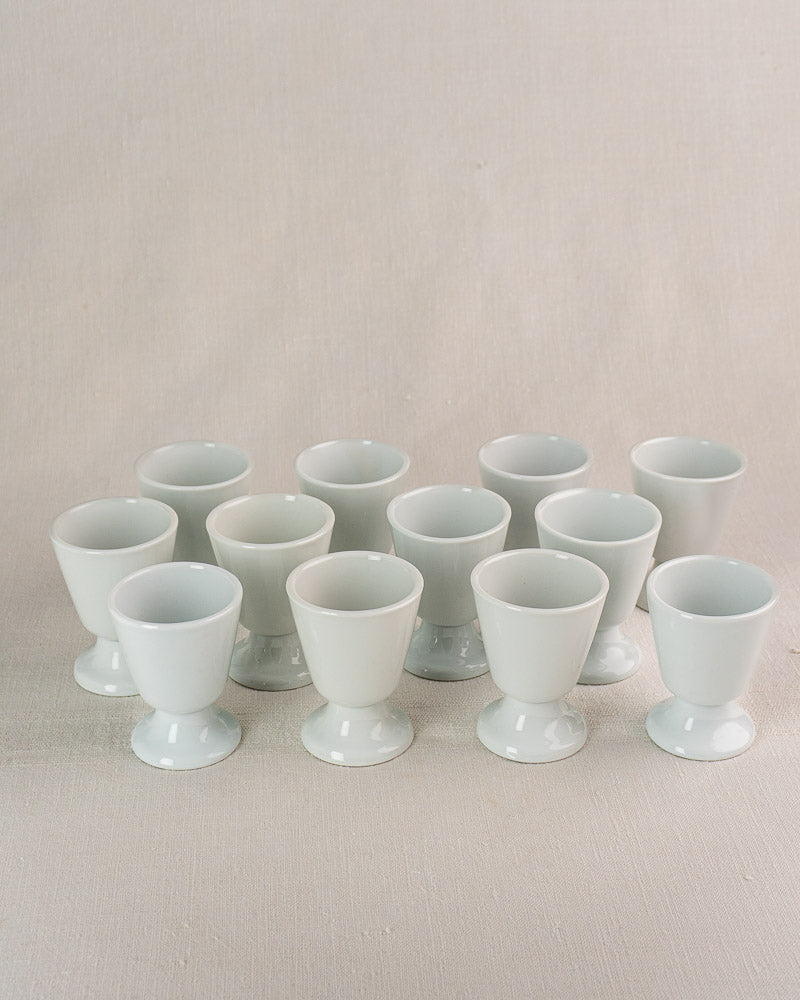 Set of twelve white porcelain mazagran coffee cups by CNP Tradition France on light textured surface.