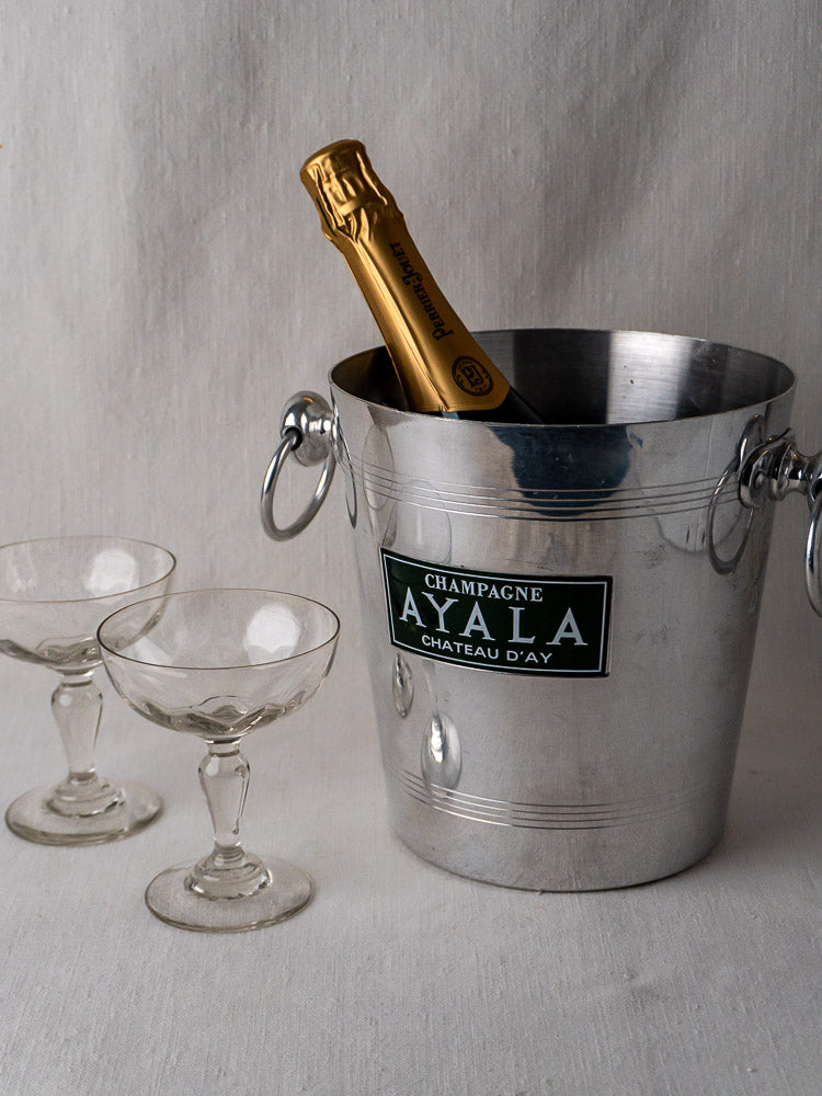 Vintage French Argit aluminum Ayala Champagne bucket with bottle and two coupe glasses on white surface.