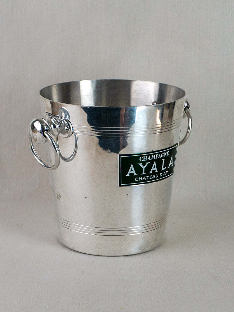 Vintage French Argit aluminum Ayala Champagne bucket with side handles and “Champagne Ayala Chateau d’Ay” label on light surface.