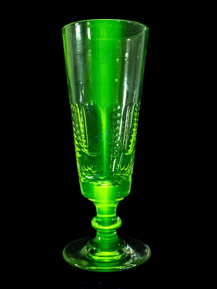 Set of six antique French uranium glass beer flutes with decorative patterns and wide bases on a light textured surface.