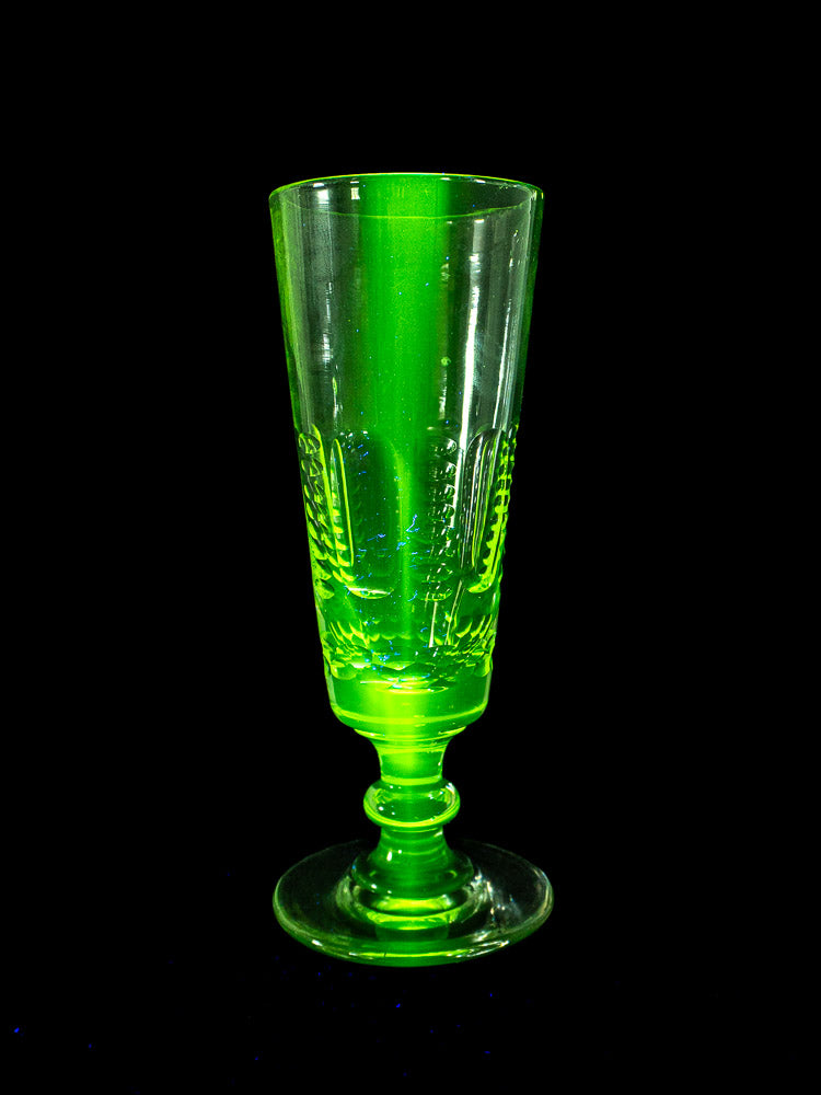 Set of six antique French uranium glass beer flutes, circa 1900, glowing green under blacklight on a black background.