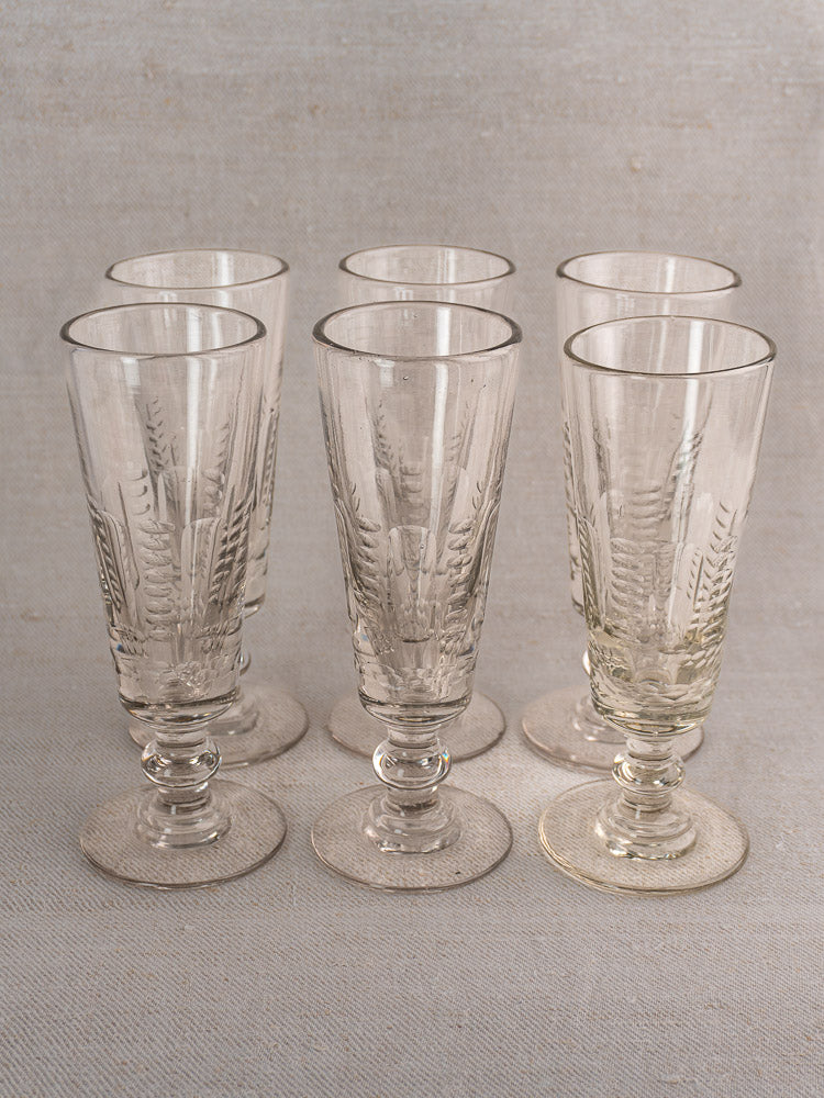 Set of six antique French uranium glass beer flutes with decorative patterns and wide bases on a light textured surface.