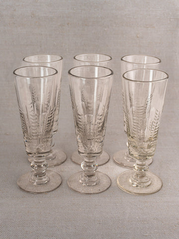 Set of six antique French uranium glass beer flutes with decorative patterns and wide bases on a light textured surface.