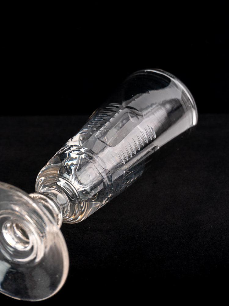 Set of six antique French uranium glass beer flutes, c.1900, with one flute resting on its side, black background.