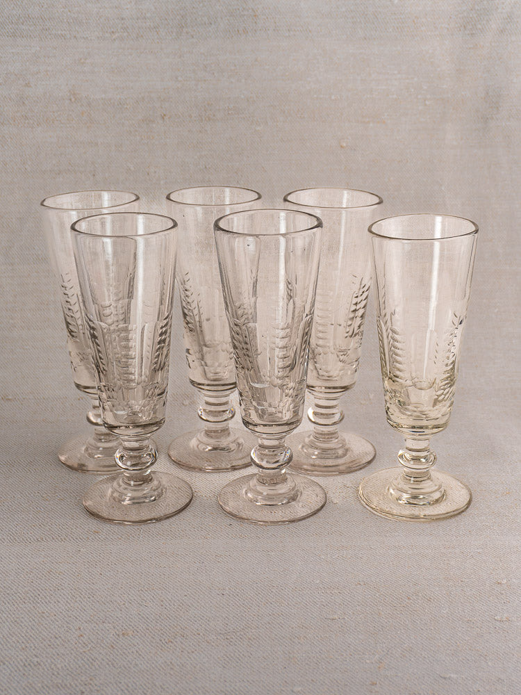 Set of six antique French uranium glass beer flutes, c.1900, with vintage patterns, arranged on a light textured surface.