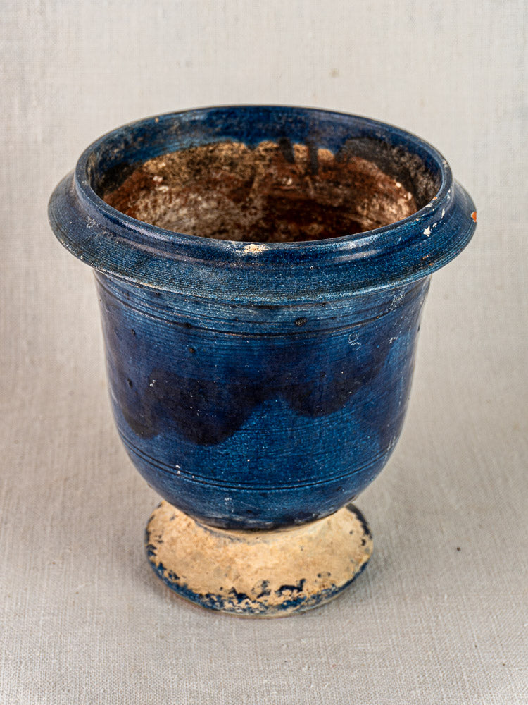 Blue glazed terracotta Medici vase with wide rim, rounded body, unglazed base on neutral fabric background.