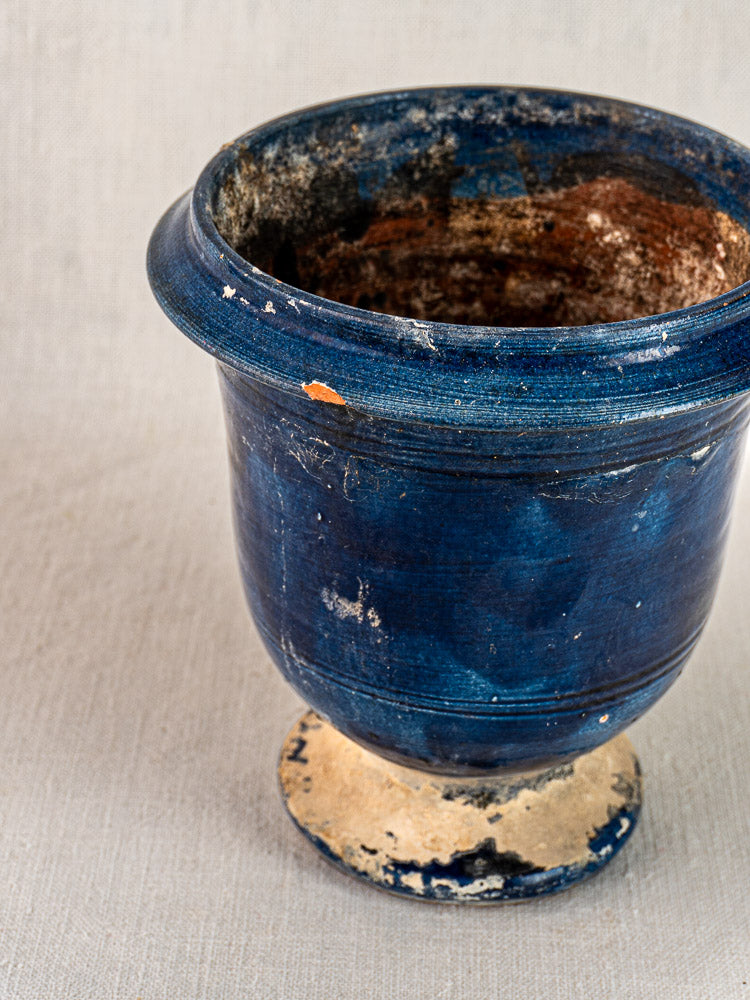 Antique French Medici vase, blue glazed terracotta with wide rim and footed base, worn and chipped on neutral fabric.