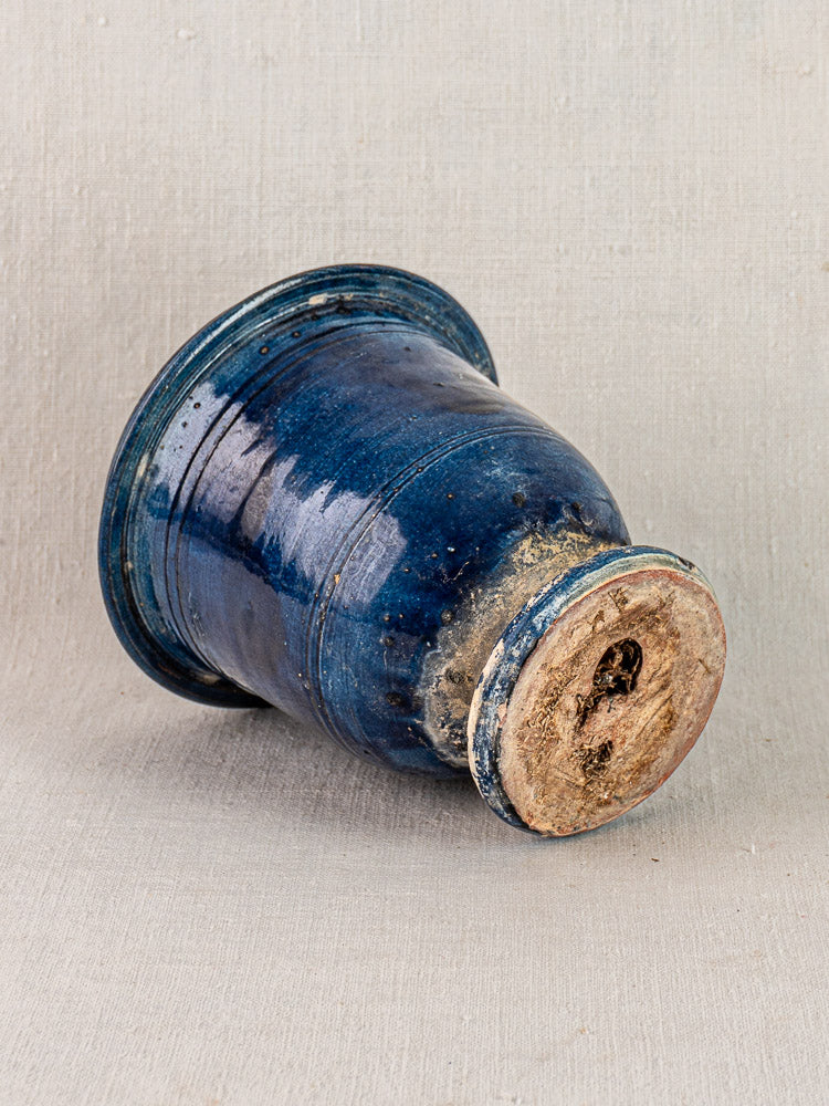 Antique French Medici vase in blue glazed terracotta with rustic unglazed base, weathered details, on neutral fabric background.