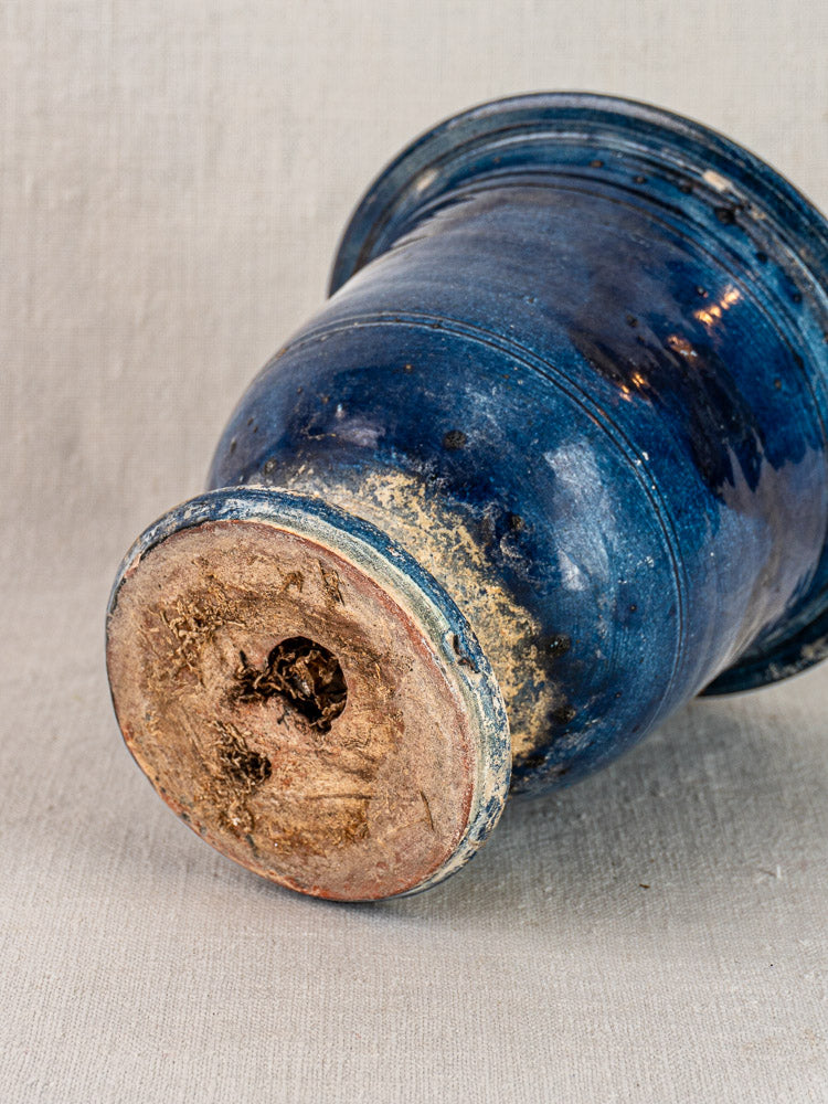 Antique French Medici vase in blue glazed terracotta, weathered base, shown on a neutral fabric background.