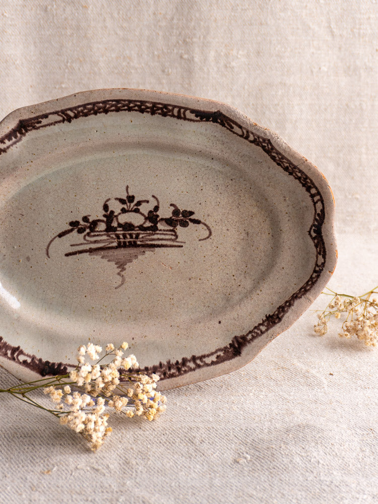 Antique French Cul Noir faience platter with brown manganese design, shown on beige fabric with dried white flowers.