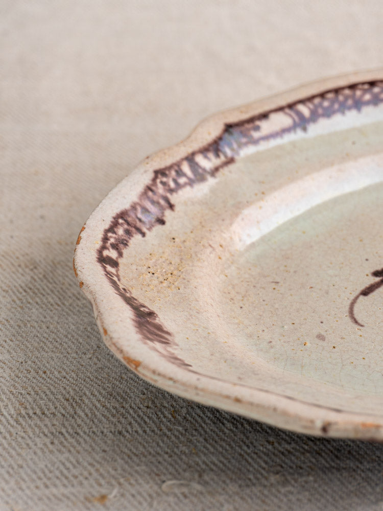 Antique French Cul Noir faience platter with wavy edge and hand-painted brown rim on textured fabric background.