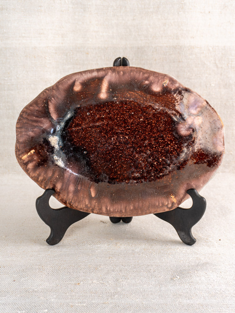 Antique French Cul Noir faience platter with brown manganese glaze displayed on a black stand, neutral fabric backdrop.